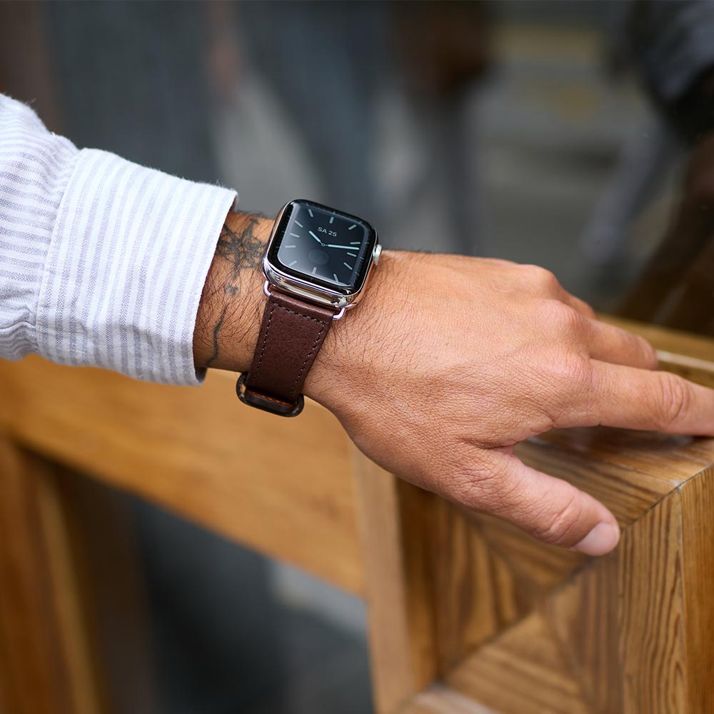Ein Mann greift an einen Türgriff und zeigt dabei seine Uhr mit Lederarmband für die Apple watch