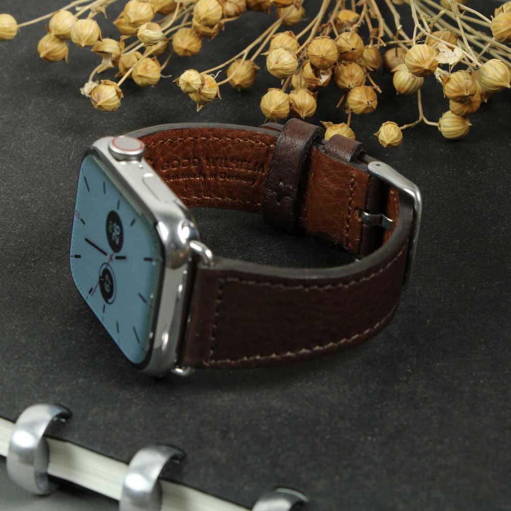 Auf einem Tisch liegt eine Apple Watch mit dunkelbraunem Lederarmband