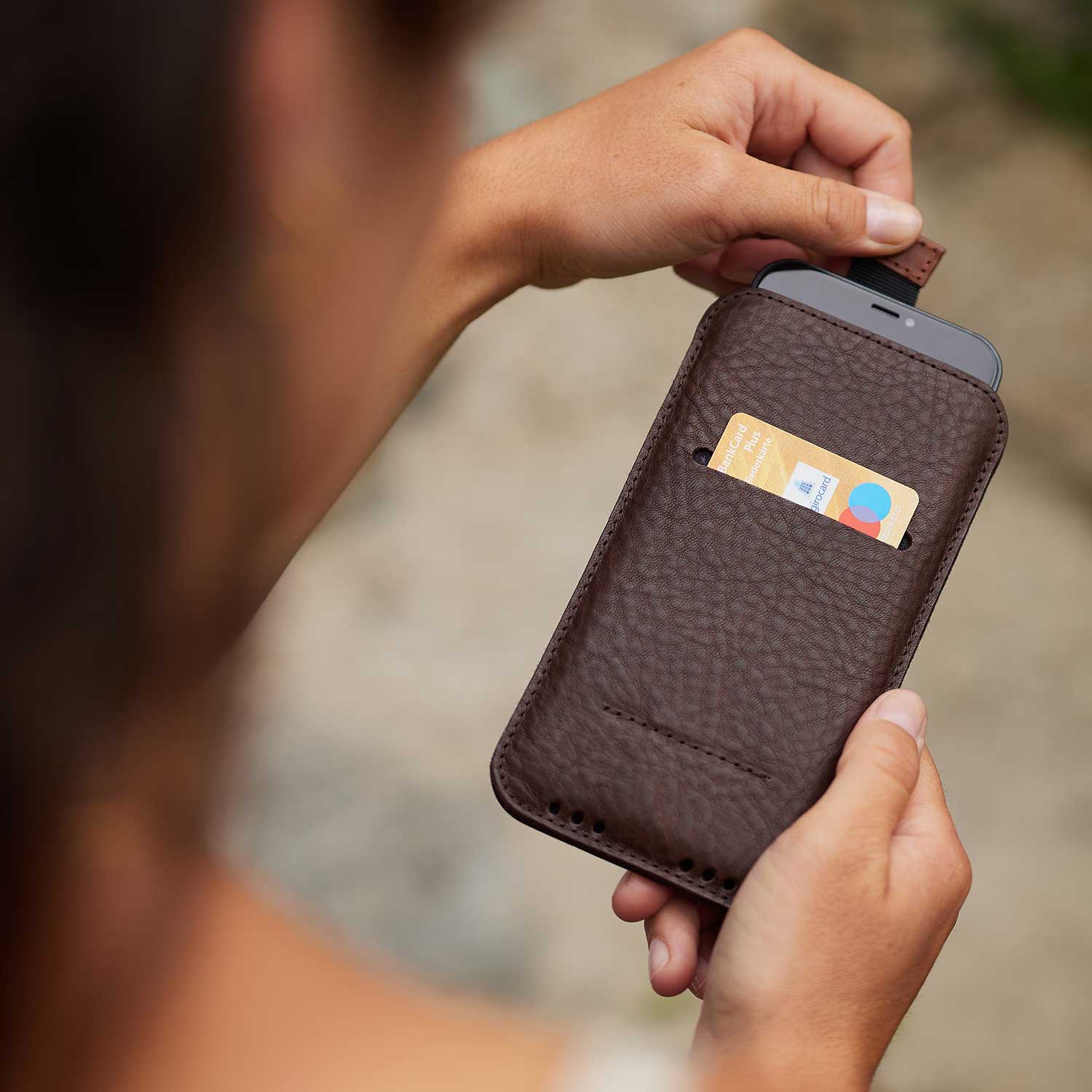 Zwei Hände halten die iPhone Hülle HEINRICH aus Leder mit Zuglasche von Goodwilhelm in der Farbe chocolate fest